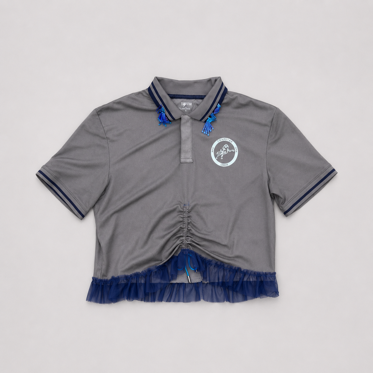 BAD BABE, polo sportswear gris upcyclé OHBAB vu de face avec tulle bleu, fronce réglable et perles brodées