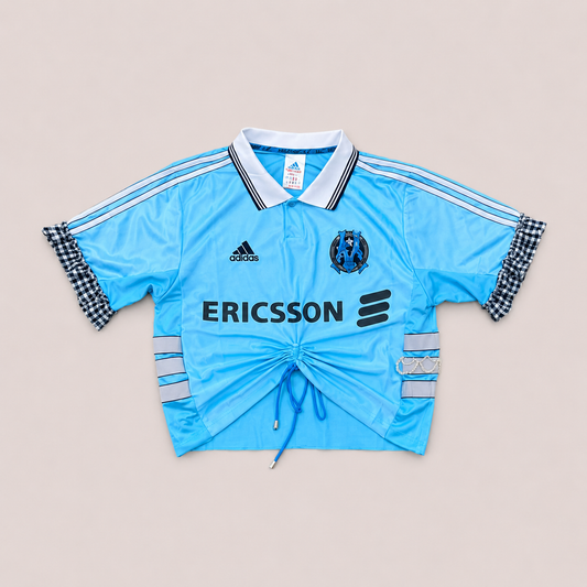 Maillot de foot bleu ciel de seconde main transformé à la main à Bayonne avec volants argentés et broderies de perles. Pièce unique OHBAB.
