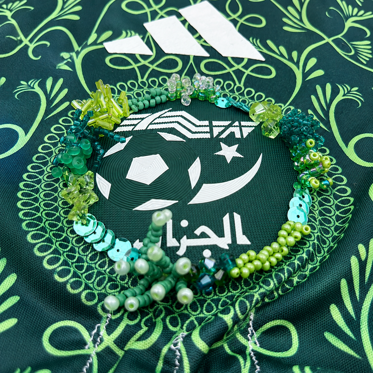 Détail des perles vertes et turquoise brodées à la main autour de l’écusson du maillot.